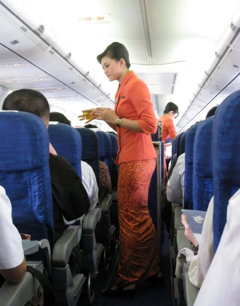 Comissários de bordo uniformizados servindo refeição a passageiros dentro da cabine de um avião