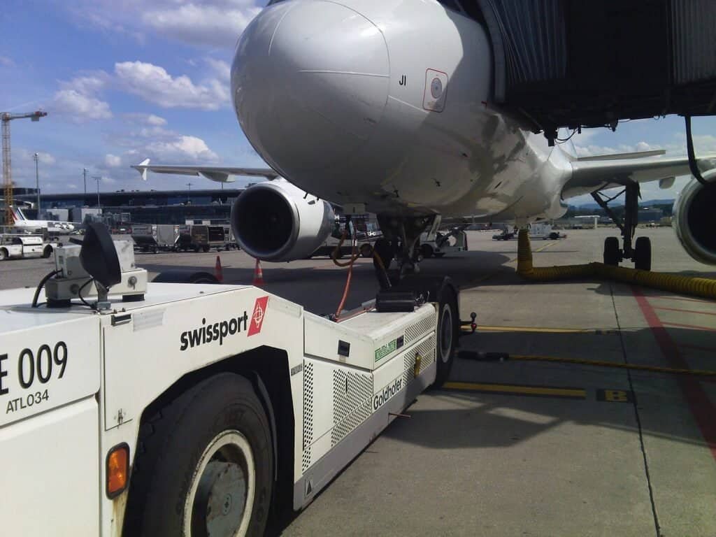 Trator de pushback amarelo da empresa de handling Swissport ao lado de um avião comercial no aeroporto de Zurique