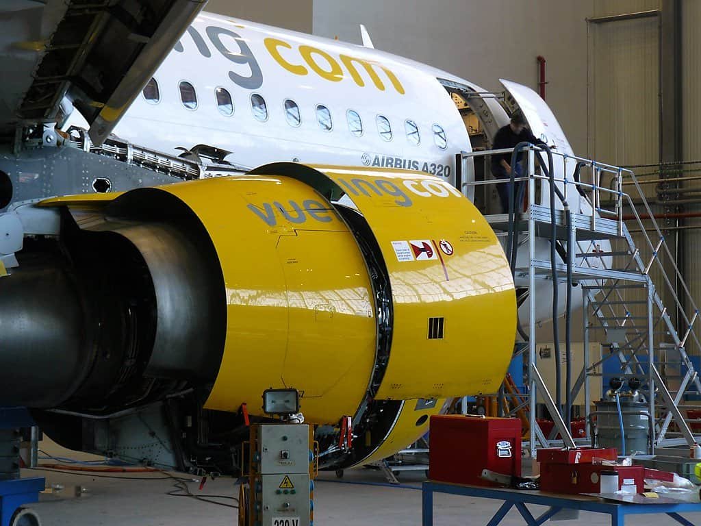 Avião Airbus A320 da Vueling dentro de um hangar de manutenção da Iberia, com painéis abertos para inspeção