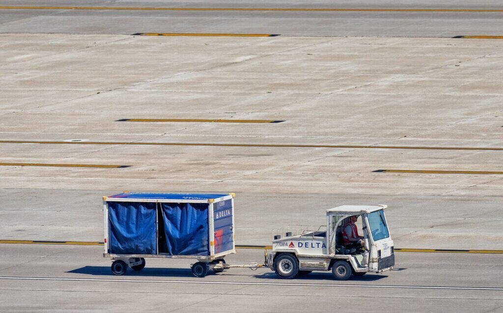Trator de bagagem da Delta Air Lines com carrinho acoplado sobre o pátio de um aeroporto