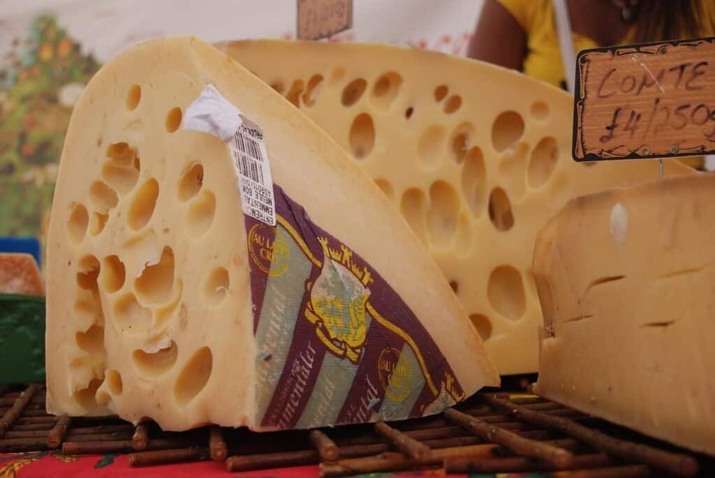Fatias de queijo tipo Emmental mostrando os furos irregulares característicos, usados como metáfora do modelo de segurança de James Reason